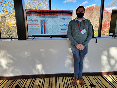 A student poses next to their poster at a poster session.